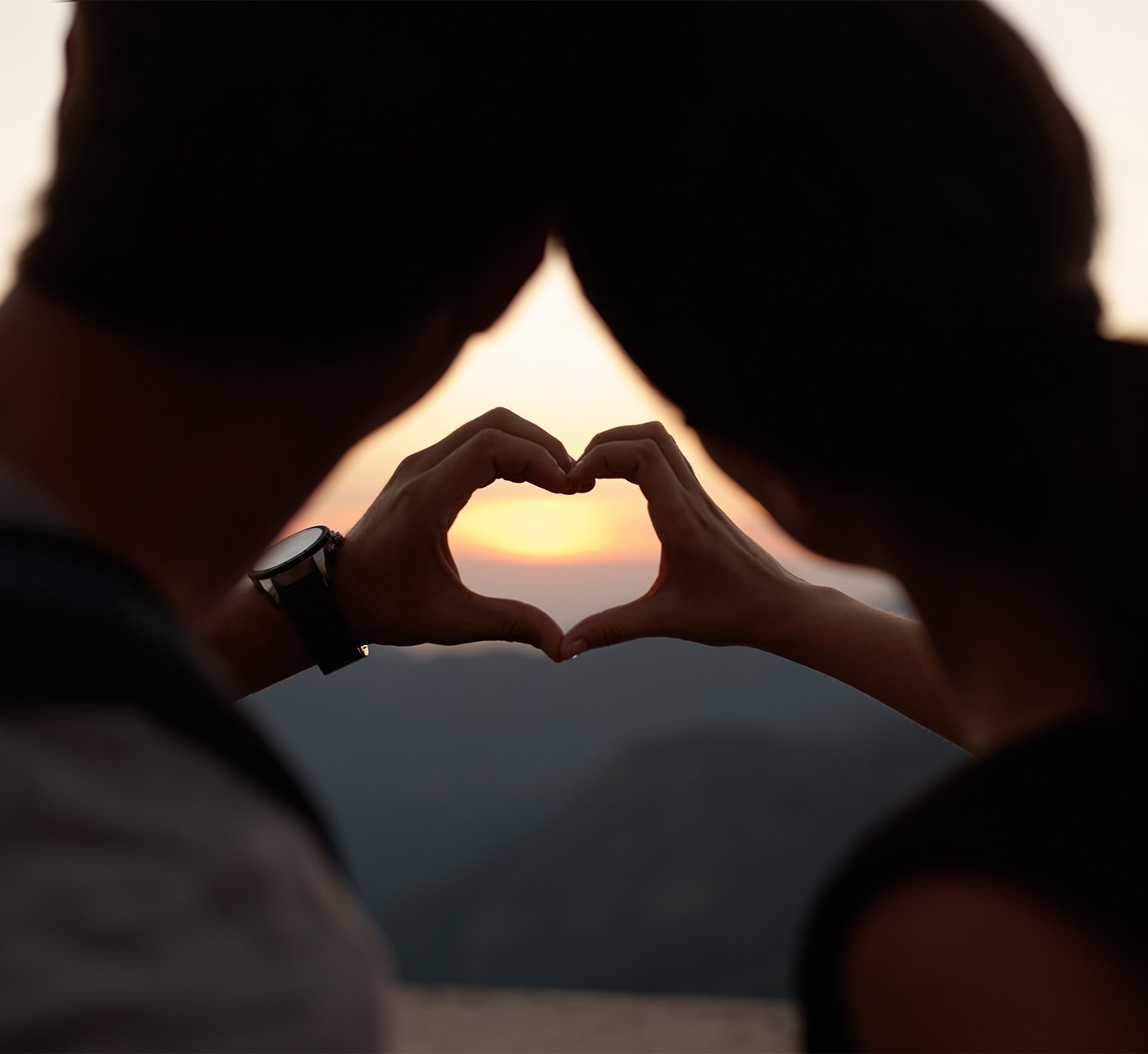Couple holding a heart with hands in sunset